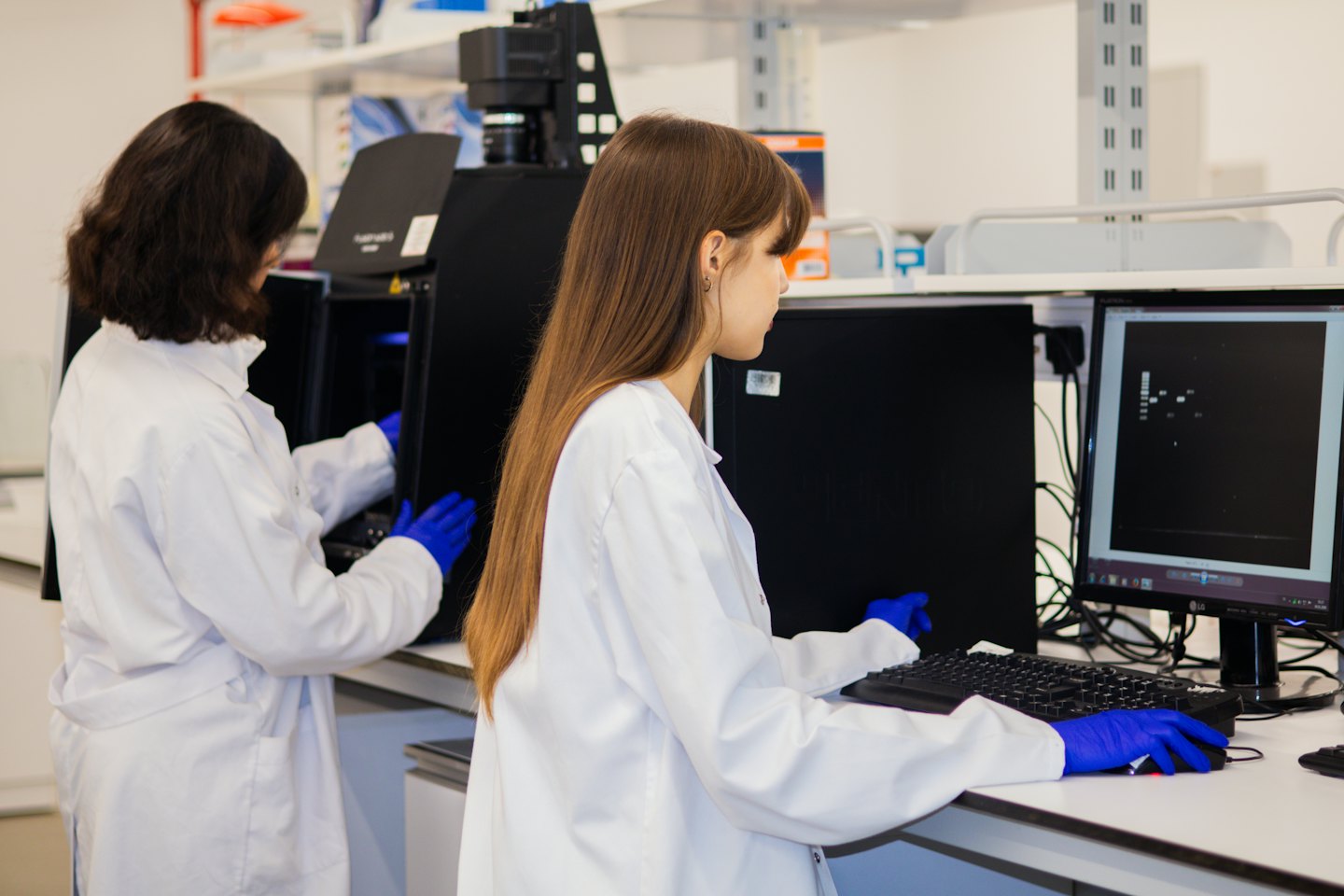Mokslininkai bendradarbiauja modernioje laboratorijoje, naudodami mokslinę įrangą ir kompiuterius.